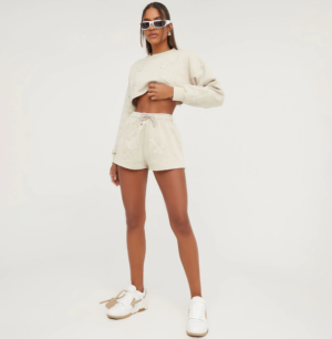 lady wearign a matching sweatshirt and sweatshorts set in beige with cross patch detail